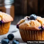 블루베리 머핀 레시피 - A close-up view of freshly baked blueberry muffins arranged on a rustic wooden table, with visible j...